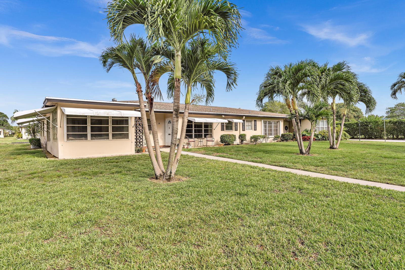 A single-story, light-colored apartment building with palm trees and a sidewalk in the foreground — 840 N High Point Blvd Boulevard N # B, Delray Beach FL 33445, DELRAY BEACH, FL