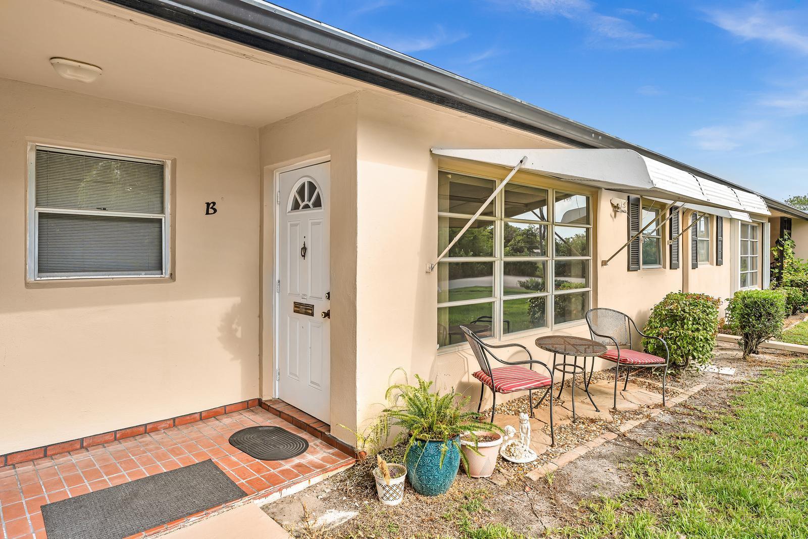The exterior of a beige building features a front door, a patio, and metal awnings — 840 N High Point Blvd Boulevard N # B, Delray Beach FL 33445, DELRAY BEACH, FL