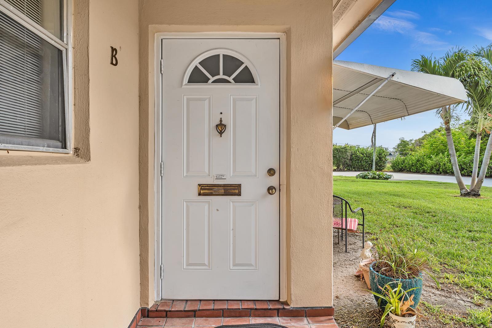 A white front door with a window and brass hardware sits on a tiled porch — 840 N High Point Blvd Boulevard N # B, Delray Beach FL 33445, DELRAY BEACH, FL