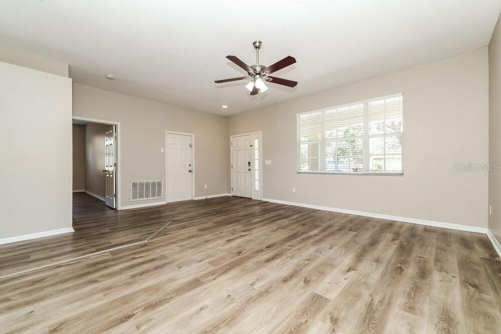 An empty living room features light-colored walls, wood-look flooring, a ceiling fan, and two doors — 6707 CAMBRIDGE PARK DRIVE, APOLLO BEACH, FL