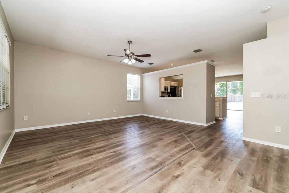 An open-concept living room features wood-look flooring, a ceiling fan, and a kitchen pass-through window — 6707 CAMBRIDGE PARK DRIVE, APOLLO BEACH, FL