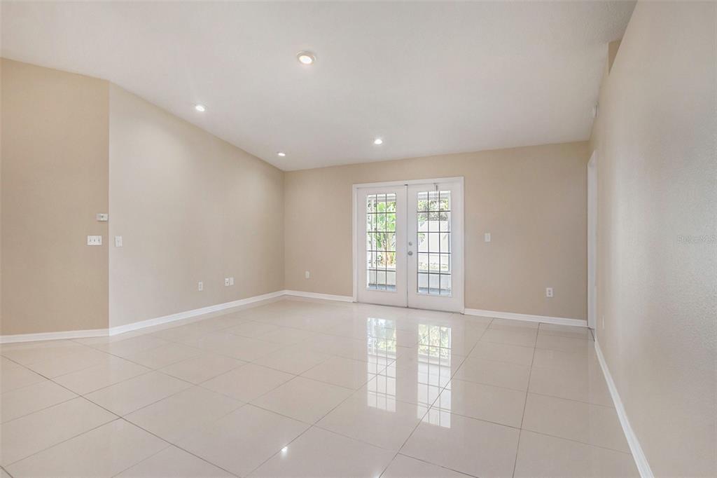 A bright, empty room features beige walls, large white floor tiles, and glass French doors — 12712 LONGCREST DRIVE, RIVERVIEW, FL