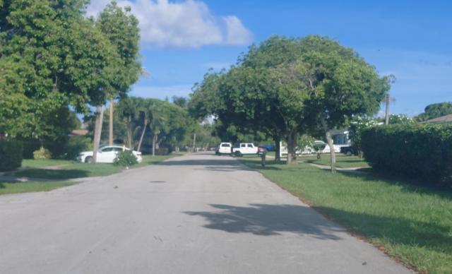 A quiet residential street lined with mature trees, green lawns, and parked cars — 200 N Ware Drive, West Palm Beach FL 33409, WEST PALM BEACH, FL