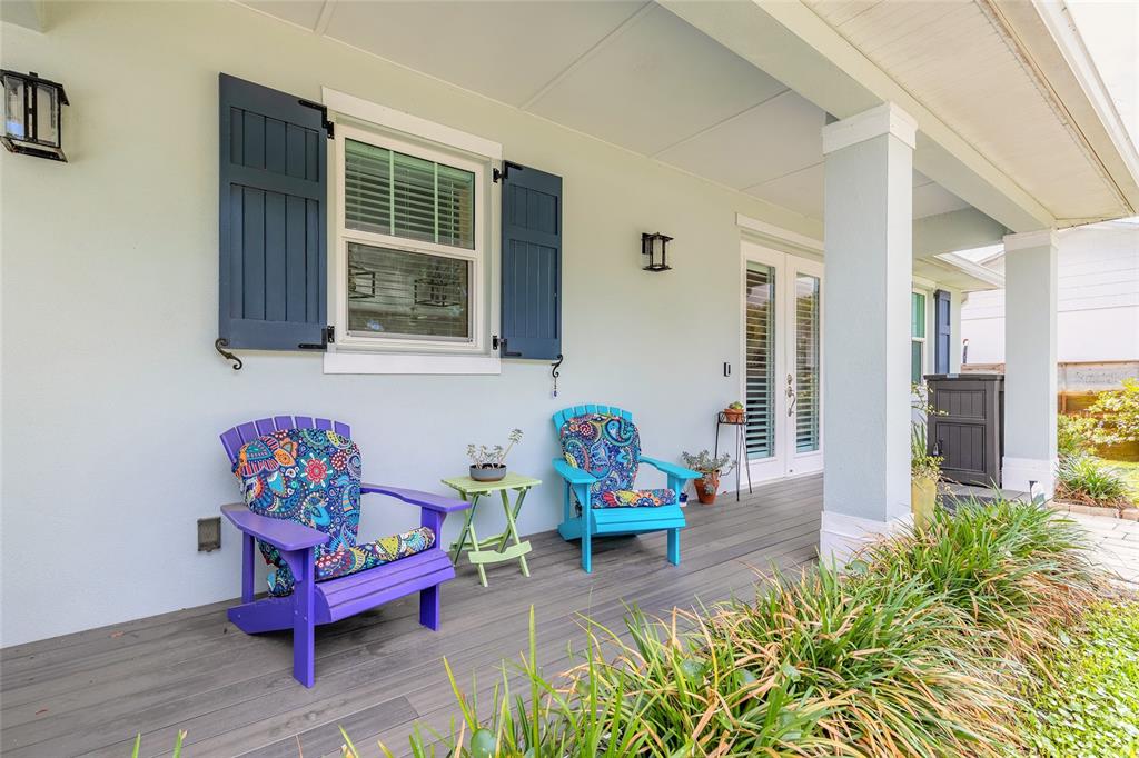 A covered porch features two colorful Adirondack chairs, a small side table, and blue shutters — 1107 S ORANGE STREET, NEW SMYRNA BEACH, FL