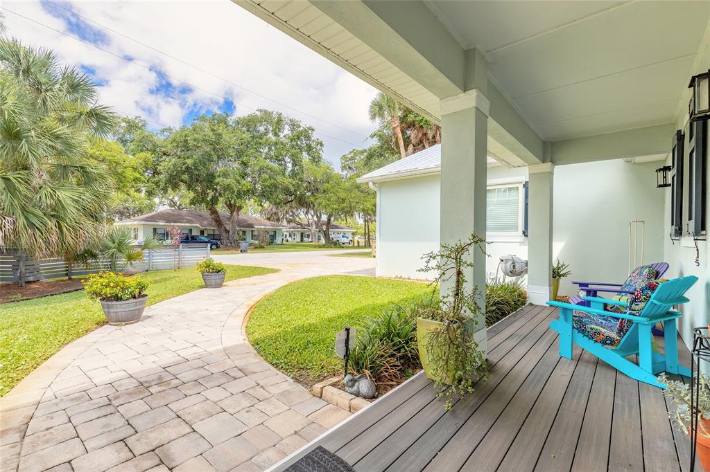 A covered porch with gray decking and two blue chairs overlooks a paved walkway and lawn — 1107 S ORANGE STREET, NEW SMYRNA BEACH, FL