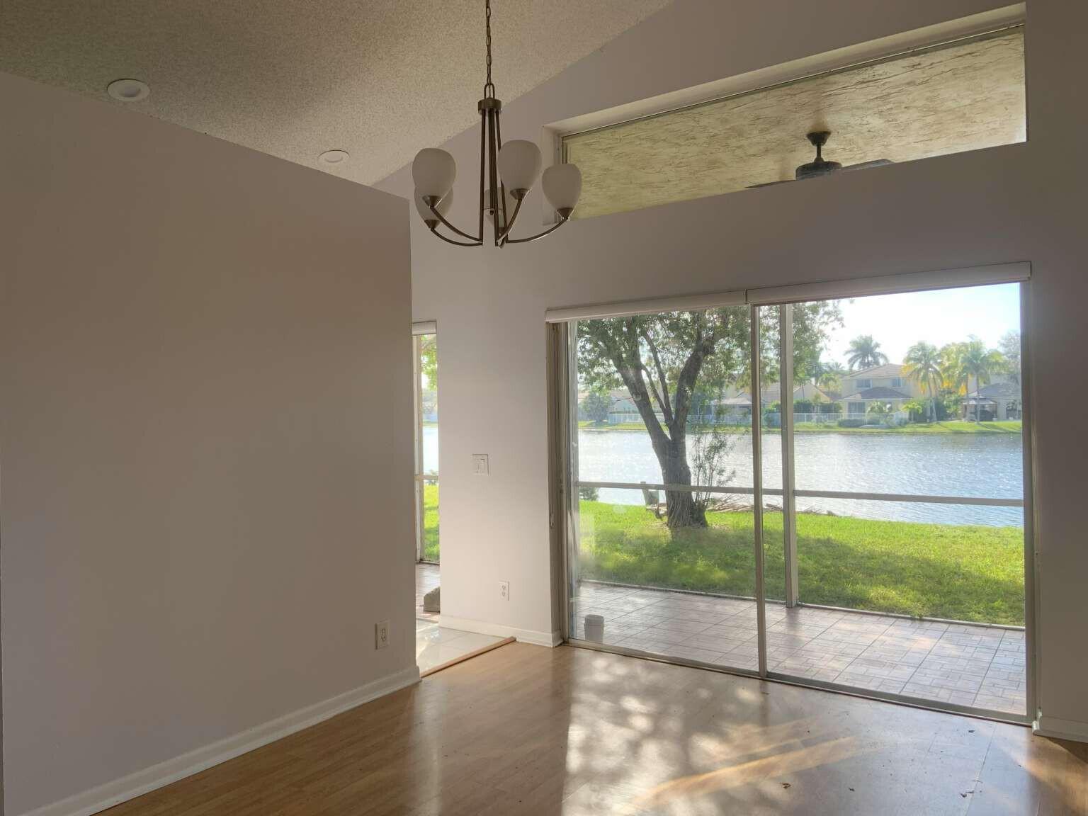 A dining area with a chandelier, hardwood floors, and sliding glass doors overlooking a lake — 856 Stanton Drive, Weston FL 33326, WESTON, FL