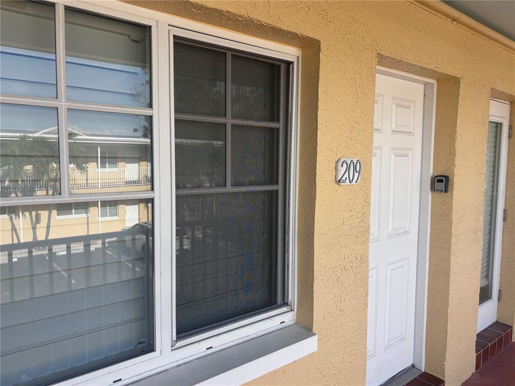 A white door labeled 209 sits next to a large window on a yellow building — 19417 GULF BOULEVARD UNIT B209, INDIAN ROCKS BEACH, FL