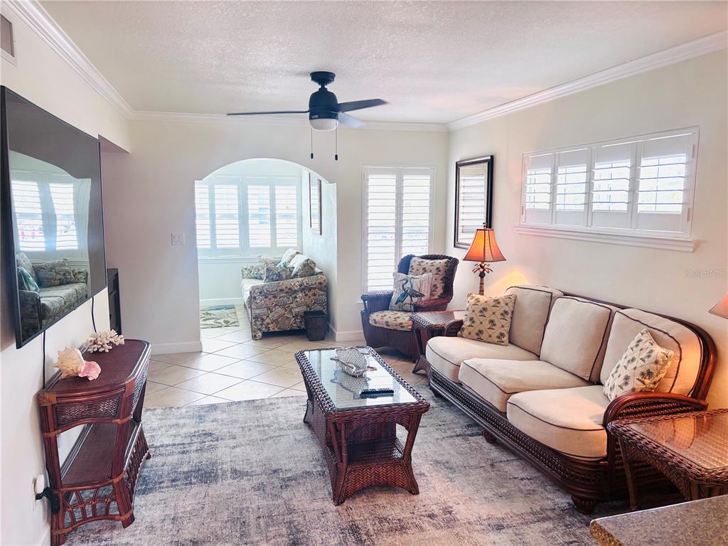 A living room features wicker furniture, a ceiling fan, and an arched opening to a sunroom — 19417 GULF BOULEVARD UNIT B209, INDIAN ROCKS BEACH, FL