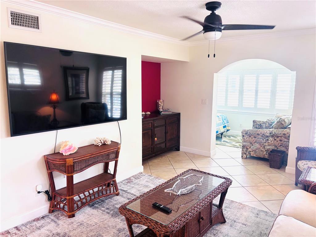 A living room features a large wall-mounted television, wicker furniture, and an arched entryway — 19417 GULF BOULEVARD UNIT B209, INDIAN ROCKS BEACH, FL