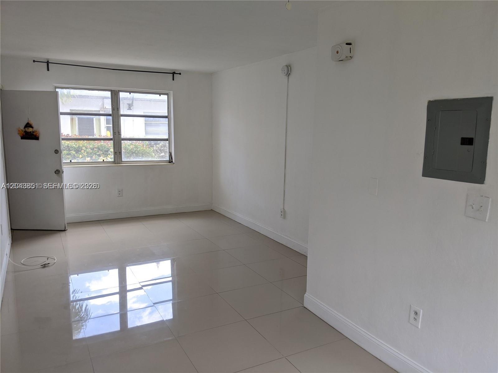 An empty room features white walls, light-colored tile flooring, a window, and an electrical panel — 7821 Byron Ave, Miami Beach FL 33141, MIAMI BEACH, FL