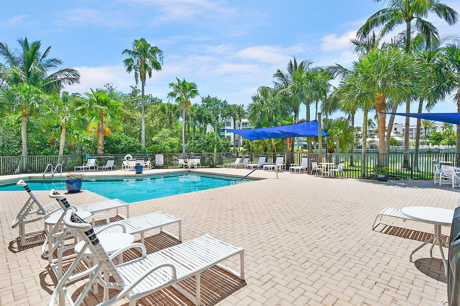 A swimming pool with lounge chairs and a blue shade sail on a paved deck — 221 NE Plantation Road # 211, Stuart FL 34996, STUART, FL