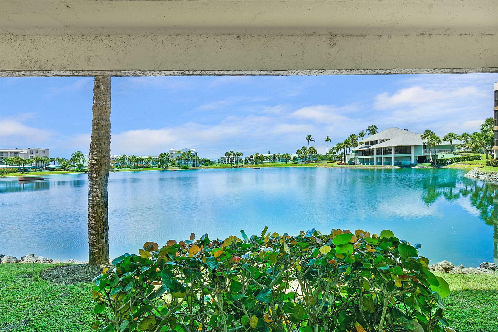 A view of a lake and surrounding buildings from a shaded patio with landscaping — 221 NE Plantation Road # 211, Stuart FL 34996, STUART, FL
