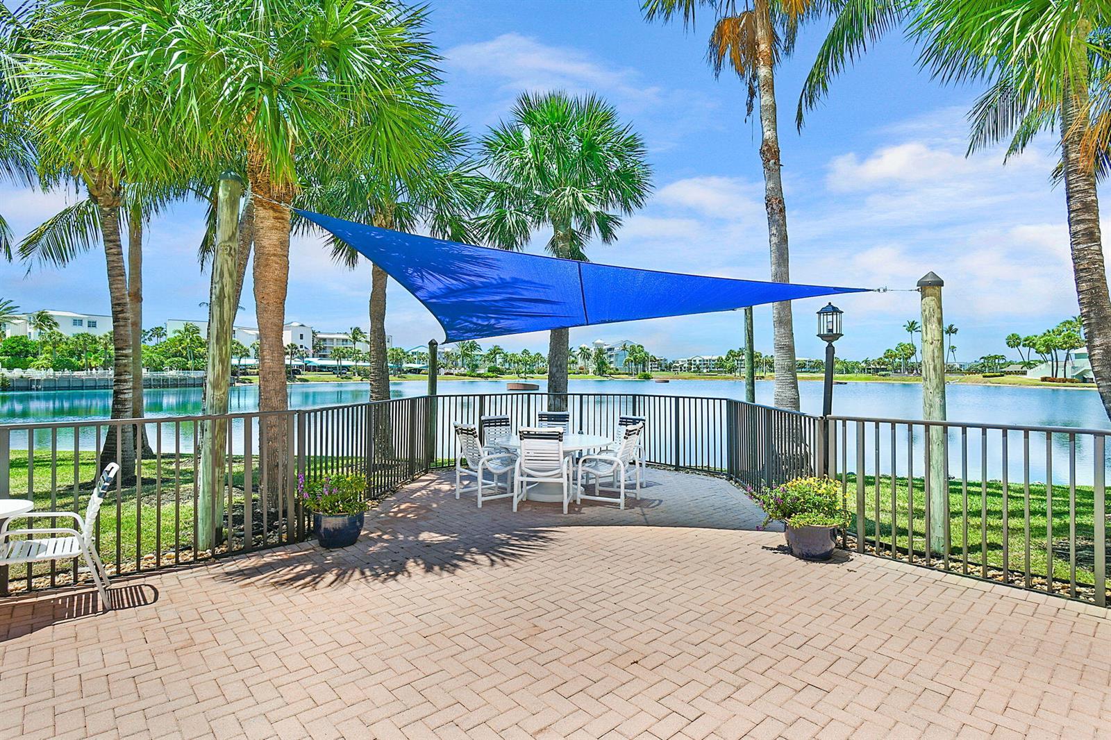 A patio with a blue shade sail, dining set, and metal fence overlooking a lake — 221 NE Plantation Road # 211, Stuart FL 34996, STUART, FL