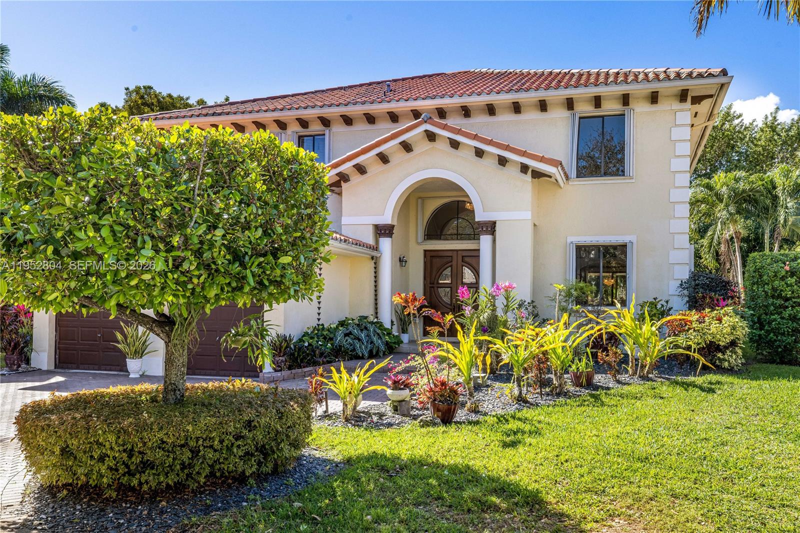 A two-story Mediterranean-style house features a tiled roof, arched entryway, and lush front landscaping — 19086 SW 76th Ave, Cutler Bay FL 33157, CUTLER BAY, FL