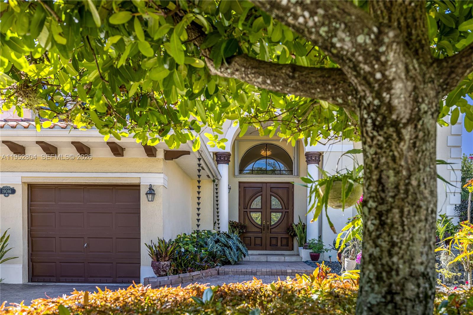 The exterior of a house features a brown garage door, arched entryway, and mature landscaping — 19086 SW 76th Ave, Cutler Bay FL 33157, CUTLER BAY, FL
