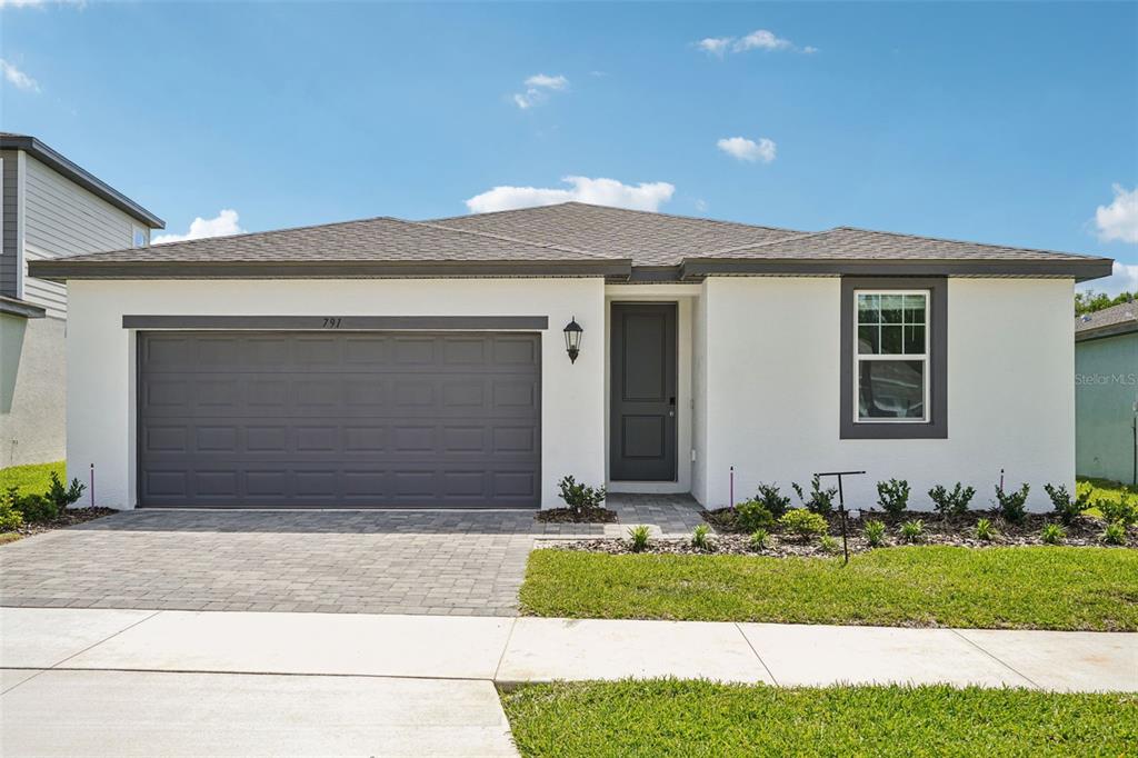 A single-story house with a white stucco exterior, gray garage door, and a paved driveway — 791 SUNSHOWER DRIVE, LADY LAKE, FL