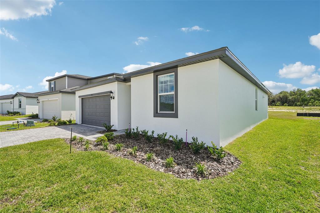 A modern, single-story house with white stucco walls, a gray garage, and a landscaped yard — 791 SUNSHOWER DRIVE, LADY LAKE, FL
