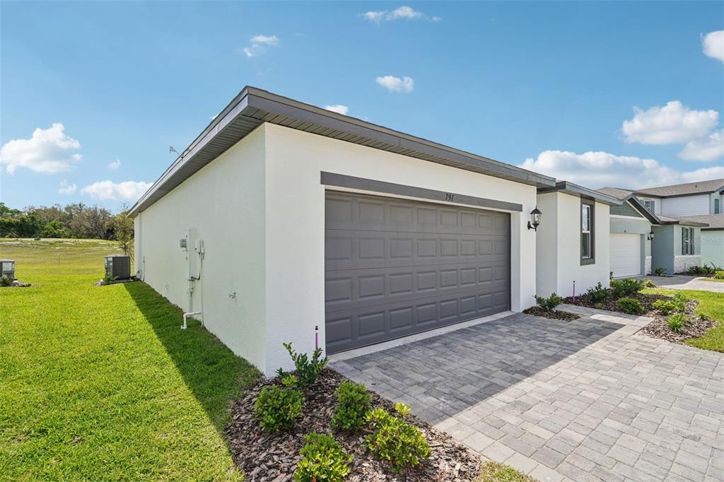 A side view of a white house with a gray garage door and paver driveway — 791 SUNSHOWER DRIVE, LADY LAKE, FL