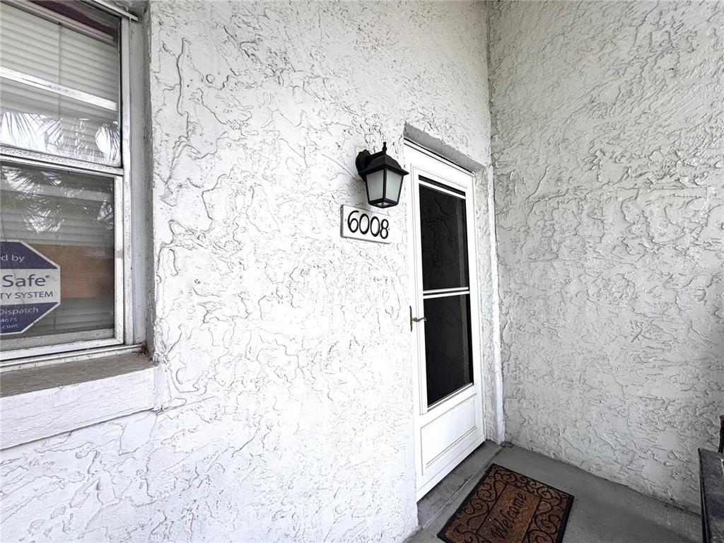 A white stucco exterior wall features a front door, a window, and a house number — 6008 AMBERLY AVENUE UNIT F63, ORLANDO, FL