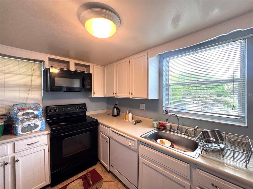 A kitchen features white cabinets, a black stove and microwave, and a stainless steel sink — 6008 AMBERLY AVENUE UNIT F63, ORLANDO, FL