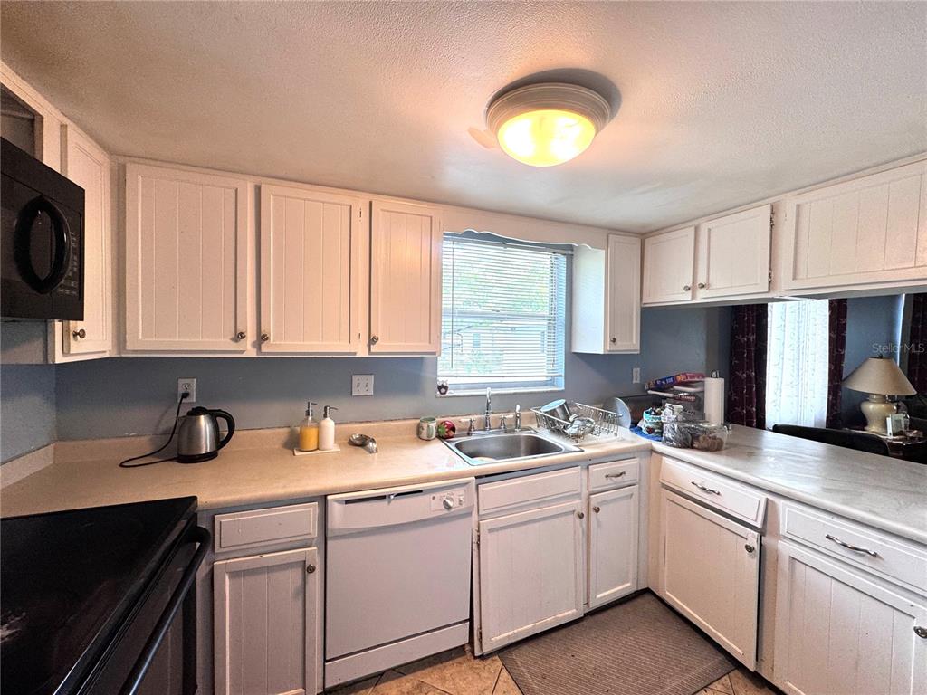 A kitchen with white cabinets, a stainless steel sink, a dishwasher, and a window — 6008 AMBERLY AVENUE UNIT F63, ORLANDO, FL