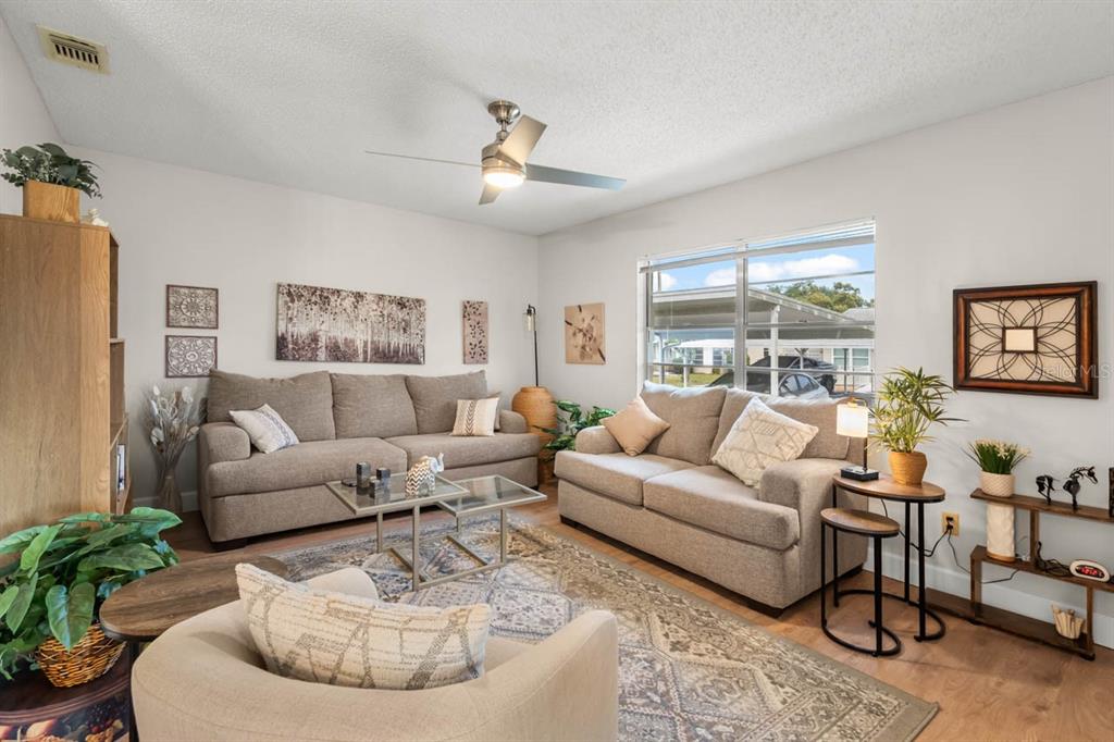 A living room features two beige sofas, a patterned area rug, and a ceiling fan — 330 GLOUCESTER BOULEVARD, SUN CITY CENTER, FL