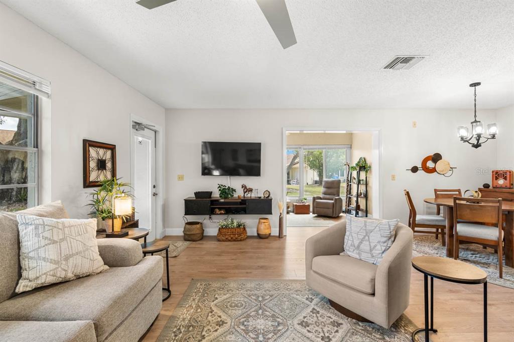 A living room with light wood floors, a television, and an adjacent dining area — 330 GLOUCESTER BOULEVARD, SUN CITY CENTER, FL