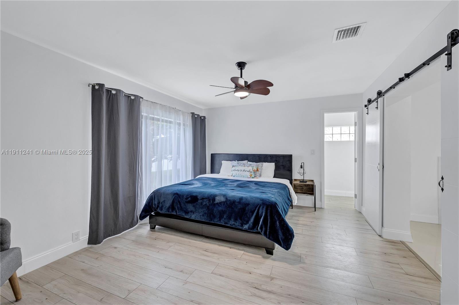 A bedroom features a dark bed, light wood-look flooring, and a sliding barn door — 217 N 31st Ave, Hollywood FL 33021, HOLLYWOOD, FL