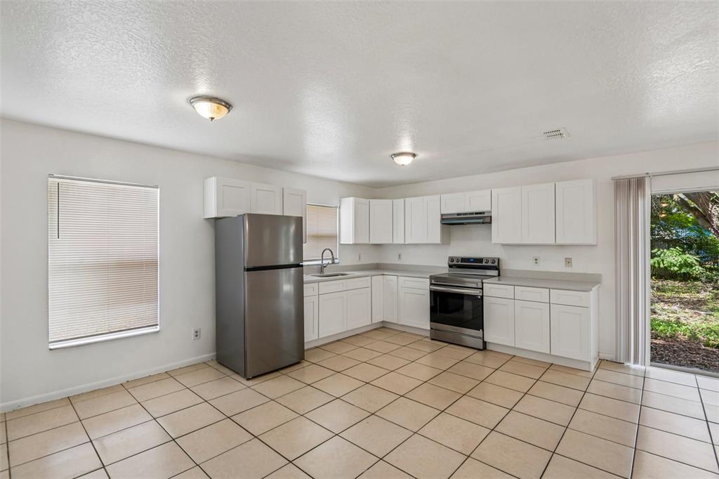 A kitchen features white cabinets, stainless steel appliances, tile flooring, and a sliding glass door — 3808 N WHITTIER STREET, TAMPA, FL