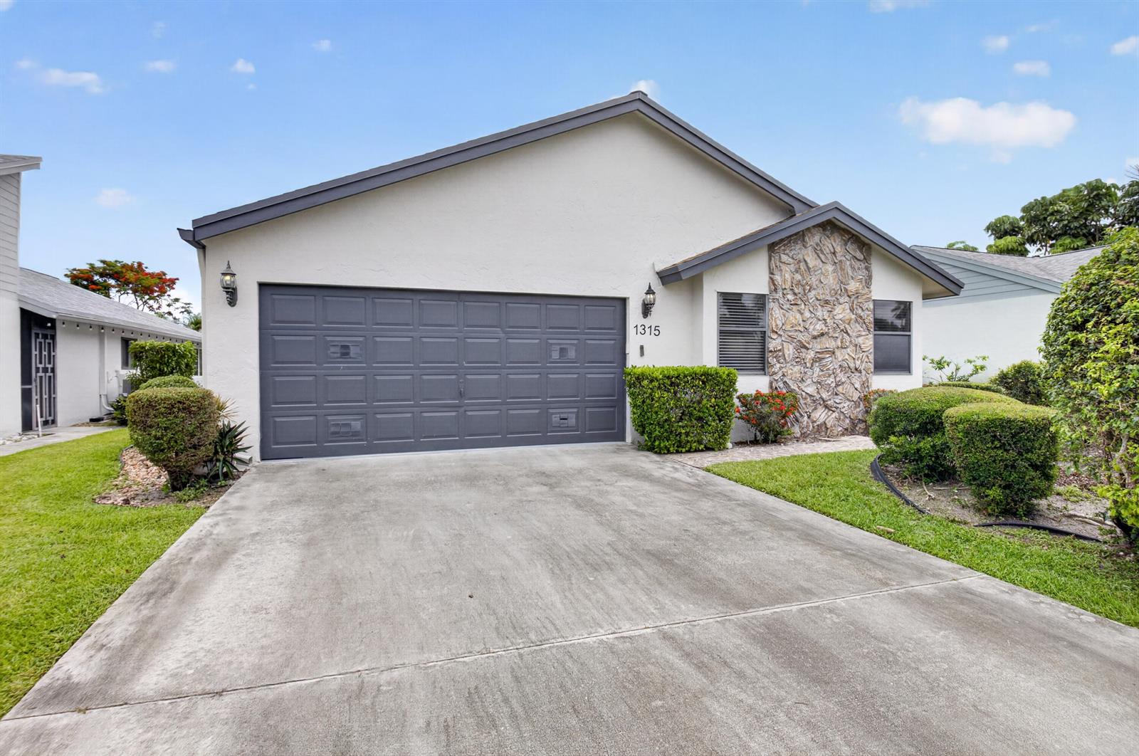 A single-story house features a gray garage door, a stone facade, and a concrete driveway — 1315 NW 25th Lane, Delray Beach FL 33445, DELRAY BEACH, FL