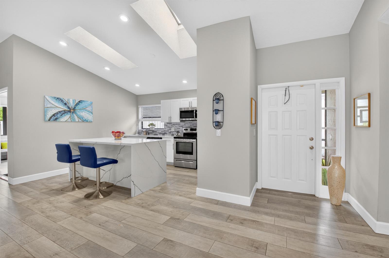 A modern kitchen features a marble-look island, white cabinets, and light wood-plank flooring — 1315 NW 25th Lane, Delray Beach FL 33445, DELRAY BEACH, FL