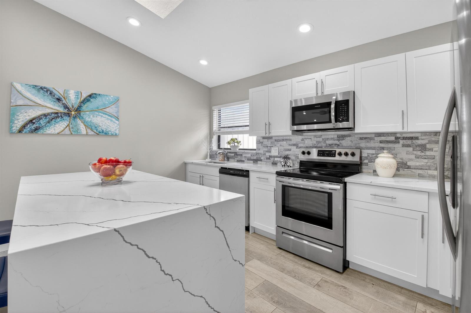 A modern kitchen features white cabinets, a marble-patterned island, and stainless steel appliances — 1315 NW 25th Lane, Delray Beach FL 33445, DELRAY BEACH, FL