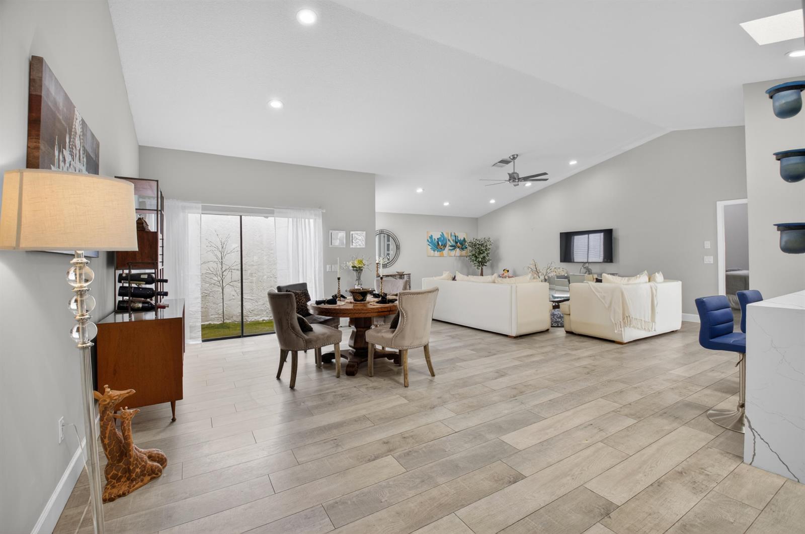 An open-concept living and dining area features light wood-look flooring and a vaulted ceiling — 1315 NW 25th Lane, Delray Beach FL 33445, DELRAY BEACH, FL