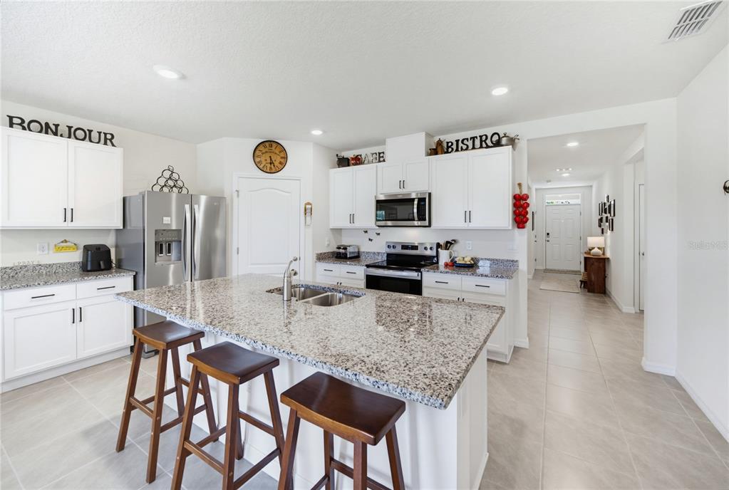 A kitchen features white cabinets, granite countertops, a center island with stools, and stainless appliances — 3432 ISLEWOOD COURT, OCOEE, FL