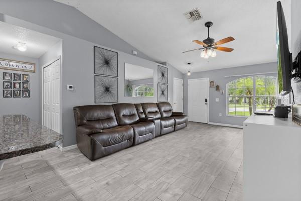 A living room features gray walls, light tile flooring, a brown leather sofa, and a ceiling fan — 2472 PINE CHASE CIRCLE, ST CLOUD, FL