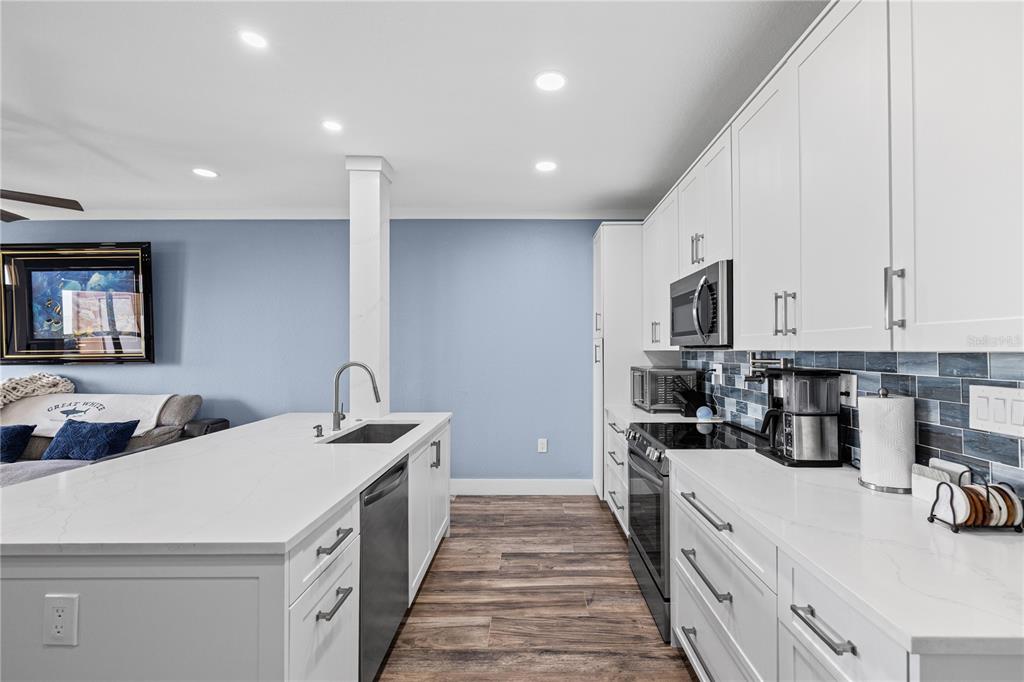 A modern kitchen features white cabinets, quartz countertops, a center island, and blue tile backsplash — 5000 CULBREATH KEY WAY UNIT 9-216, TAMPA, FL