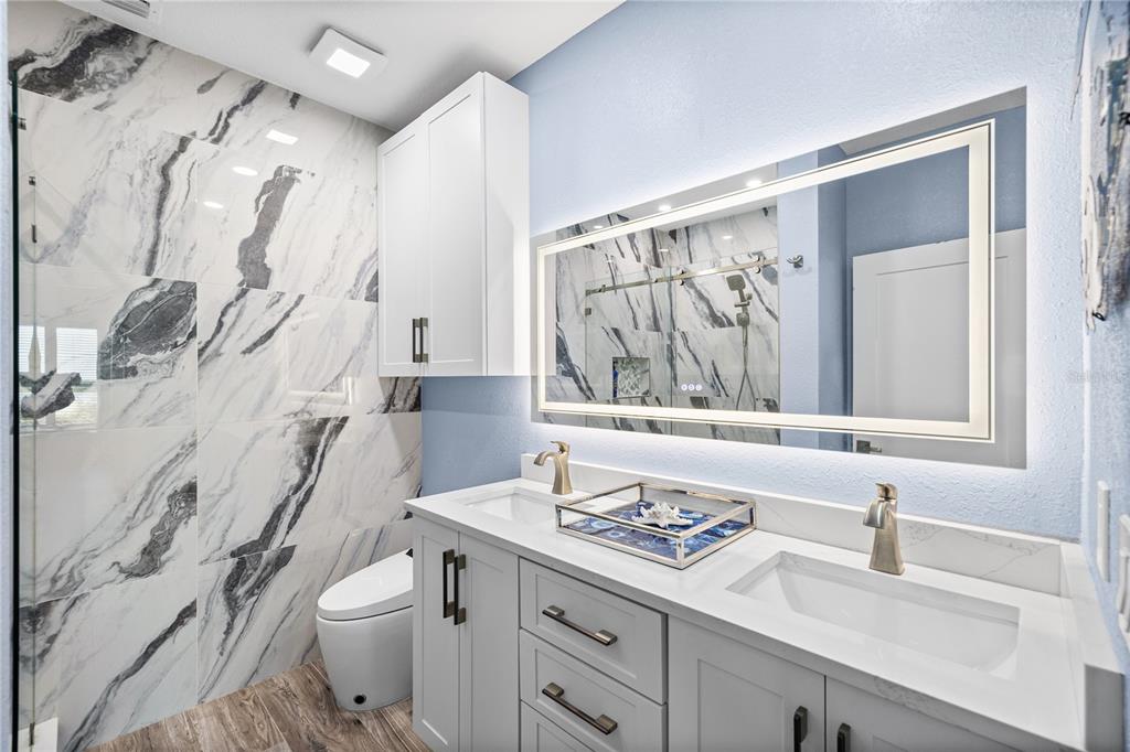 A modern bathroom features a double vanity, a large backlit mirror, and marble-patterned shower tiles — 5000 CULBREATH KEY WAY UNIT 9-216, TAMPA, FL