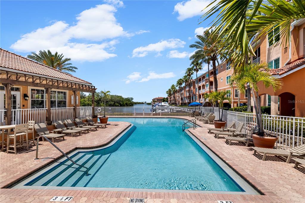 A swimming pool with lounge chairs sits on a brick patio beside a multi-story building — 5000 CULBREATH KEY WAY UNIT 9-216, TAMPA, FL