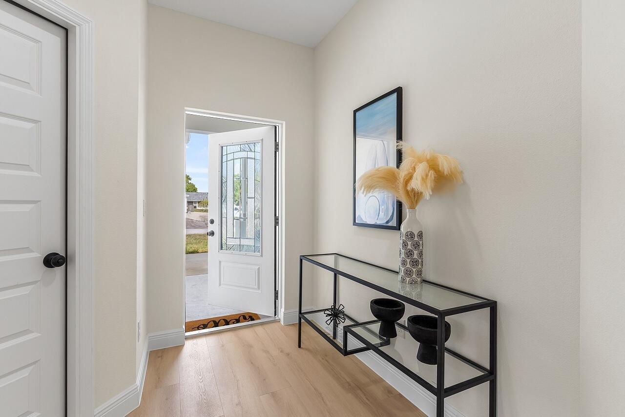 An entryway features light wood flooring, a glass-topped console table, and an open front door — 8236 104th Court, Vero Beach FL 32967, VERO BEACH, FL