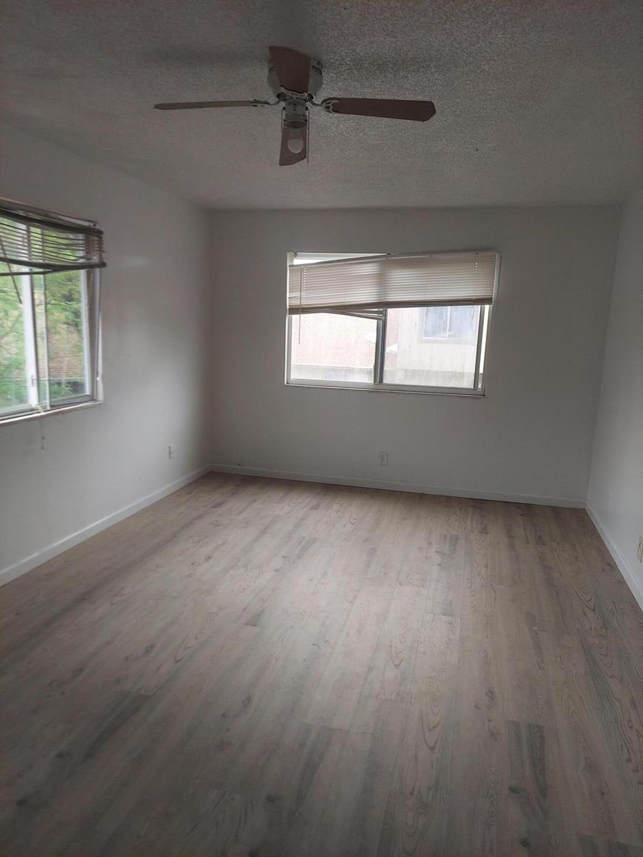 An empty bedroom with light wood-look flooring, white walls, a ceiling fan, and two windows — 2215 NW 56th Avenue # e, Lauderhill FL 33313, LAUDERHILL, FL
