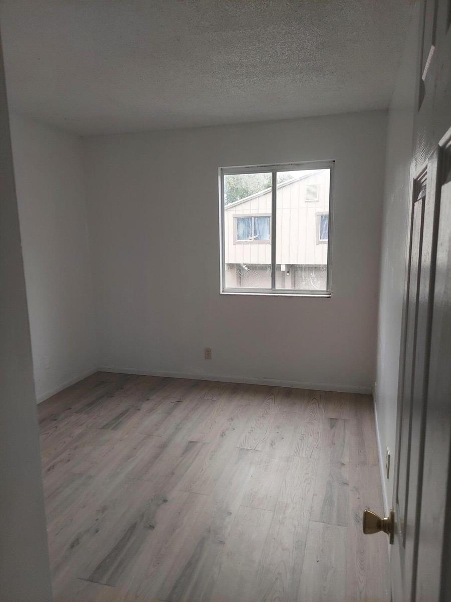 An empty bedroom features light-colored wood-look flooring, white walls, and a single window — 2215 NW 56th Avenue # e, Lauderhill FL 33313, LAUDERHILL, FL