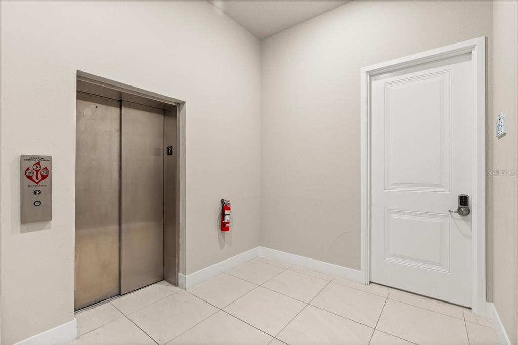 A hallway features a stainless steel elevator, a fire extinguisher, and a white door — 7770 SANDY RIDGE DRIVE 218 BLDG 28 With Elevator, KISSIMMEE, FL