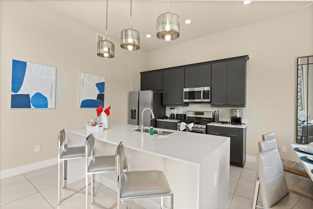 A modern kitchen features dark gray cabinetry, a white quartz island, and three pendant lights — 7770 SANDY RIDGE DRIVE 218 BLDG 28 With Elevator, KISSIMMEE, FL