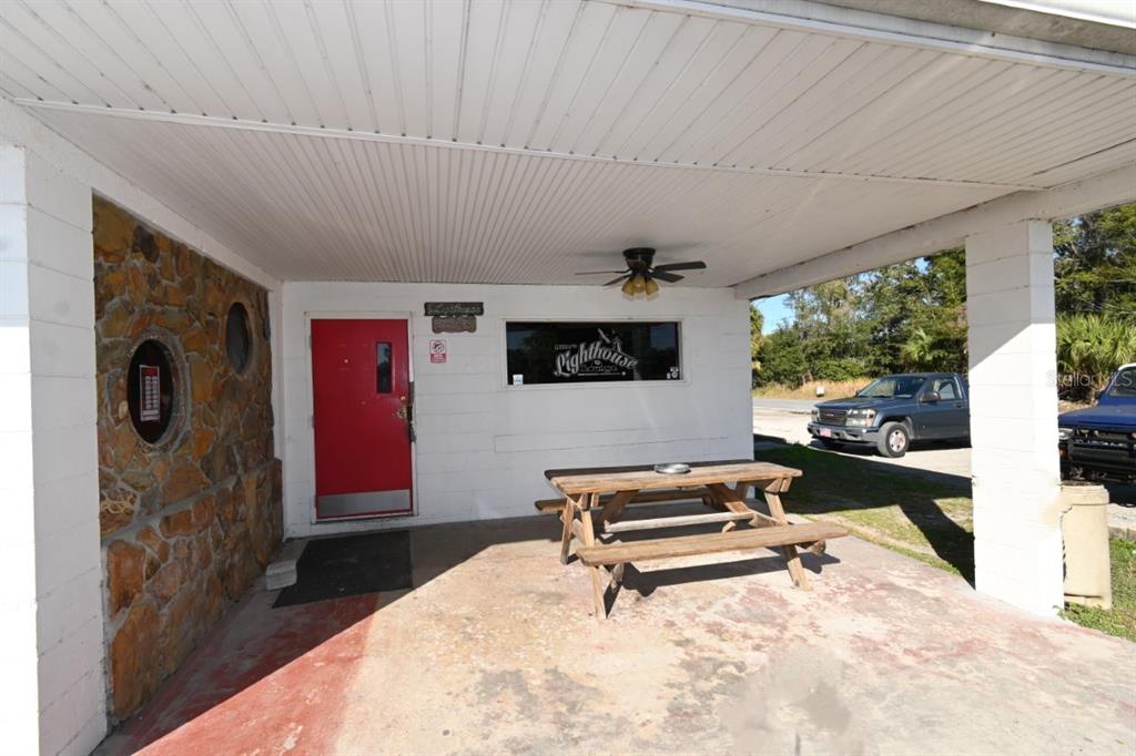 A covered patio features a picnic table, a red door, and a stone-accented wall — 5025 TREIMAN BOULEVARD, DADE CITY, FL