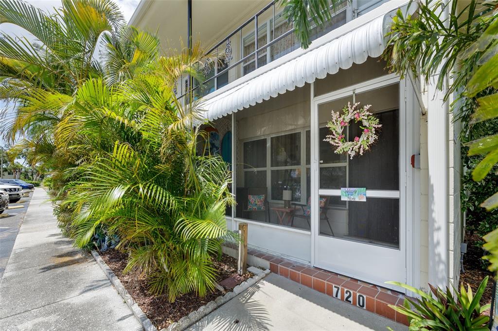 A ground-level apartment entrance features a screened-in porch, a floral wreath, and tropical landscaping — 4154 56TH STREET N UNIT 720, KENNETH CITY, FL
