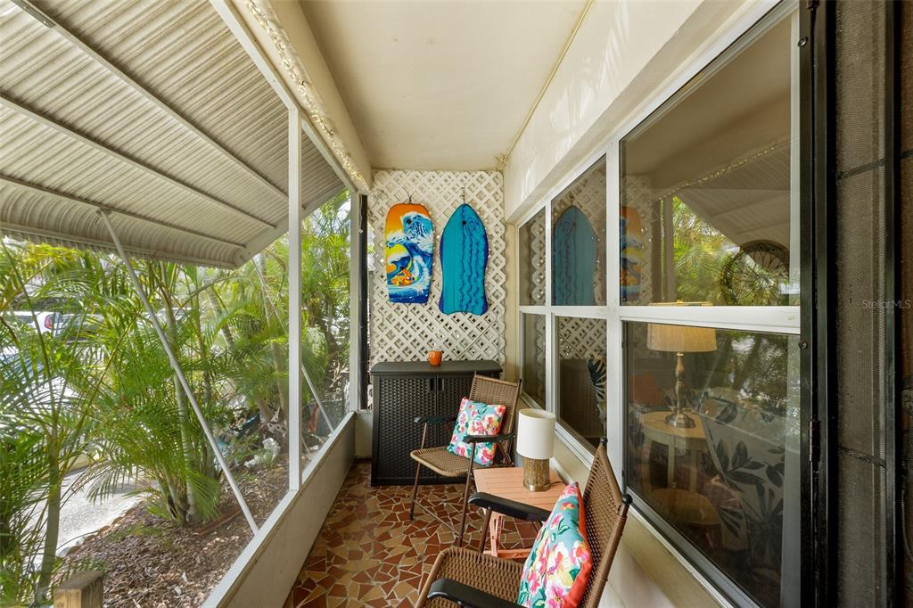 A screened-in porch features tiled flooring, wicker chairs, and two bodyboards mounted on lattice — 4154 56TH STREET N UNIT 720, KENNETH CITY, FL