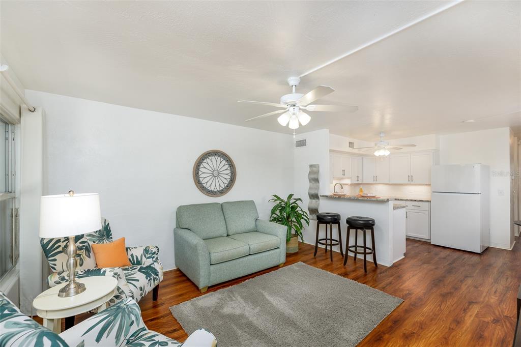 A living room with a green sofa, patterned armchair, and an open kitchen with bar seating — 4154 56TH STREET N UNIT 720, KENNETH CITY, FL