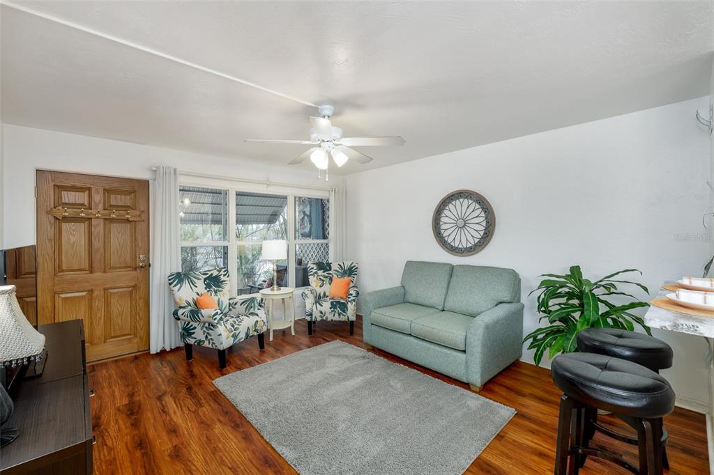 A living room features wood-look flooring, a light green sofa, two patterned chairs, and a ceiling fan — 4154 56TH STREET N UNIT 720, KENNETH CITY, FL