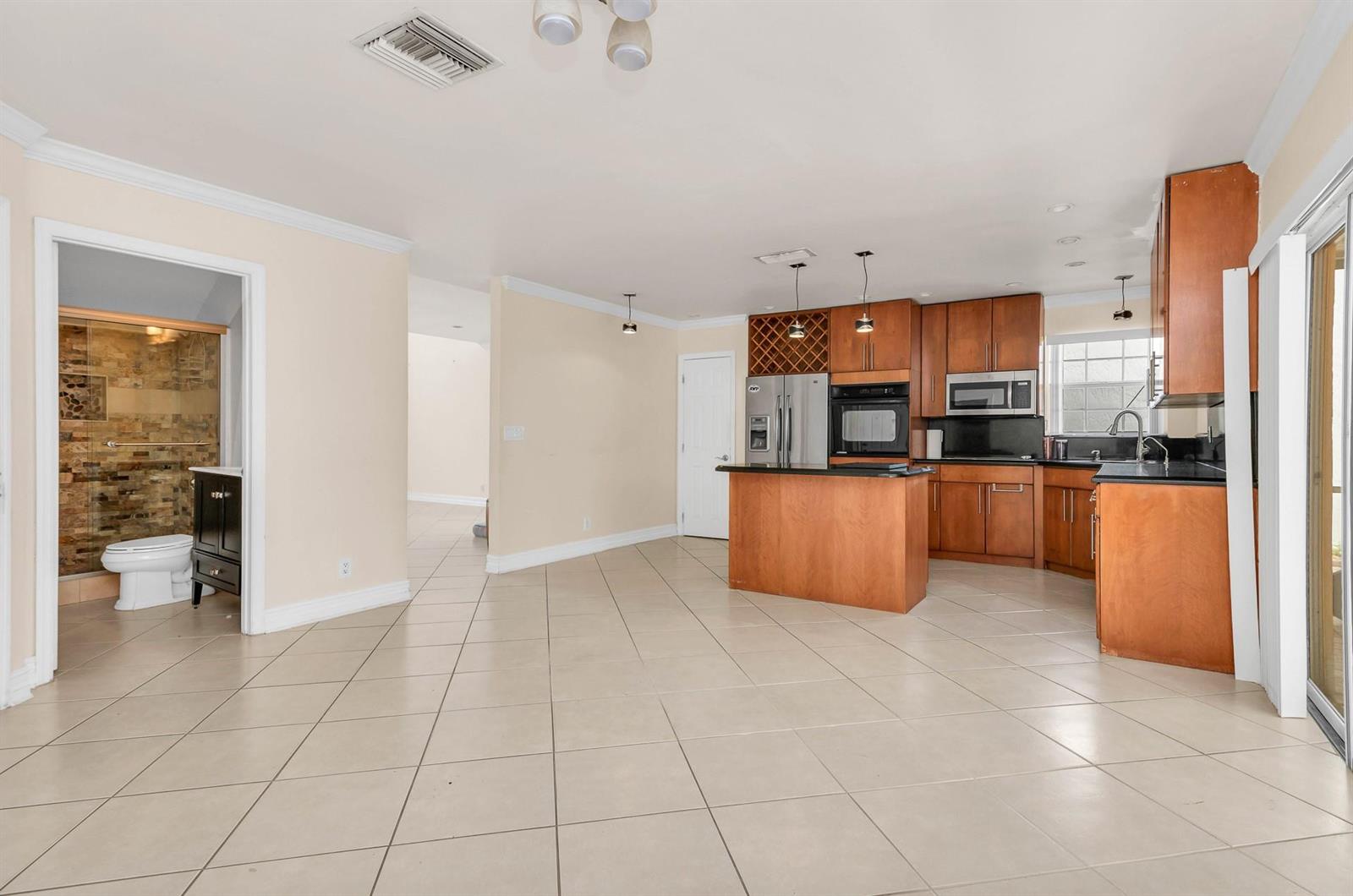 A kitchen with wood cabinets and a central island opens to a tiled living area — 5486 NW 44th Way, Coconut Creek FL 33073, COCONUT CREEK, FL