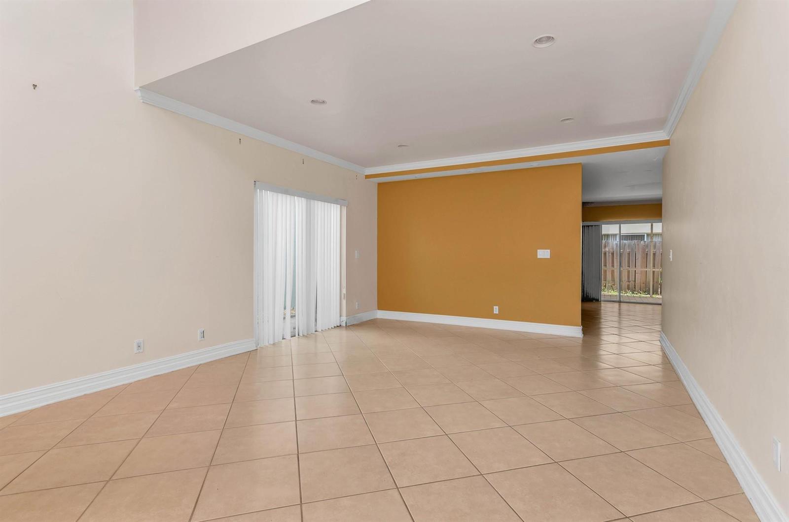 An empty living room features beige tile floors, a mustard-colored accent wall, and sliding doors — 5486 NW 44th Way, Coconut Creek FL 33073, COCONUT CREEK, FL